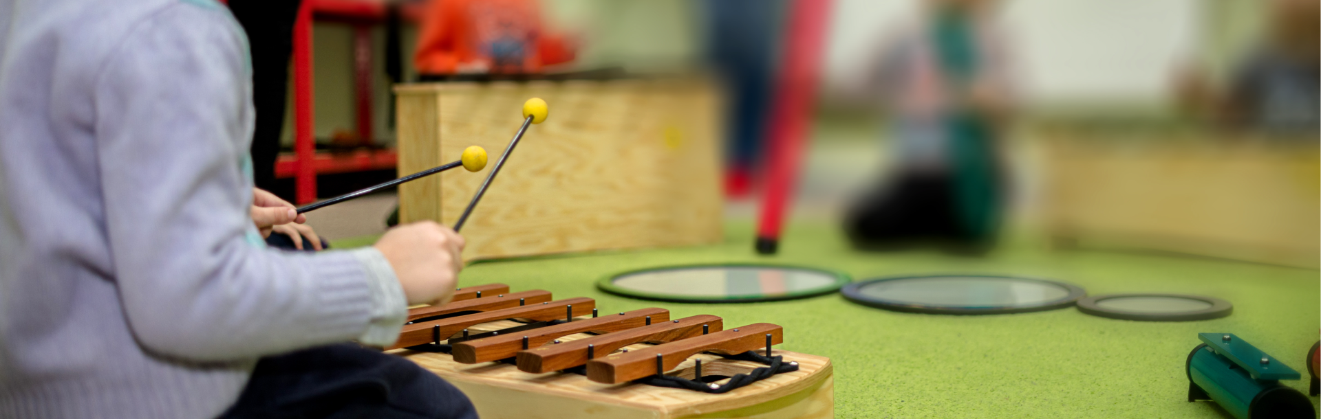 Kids sitting on a green rug playing musical instruments