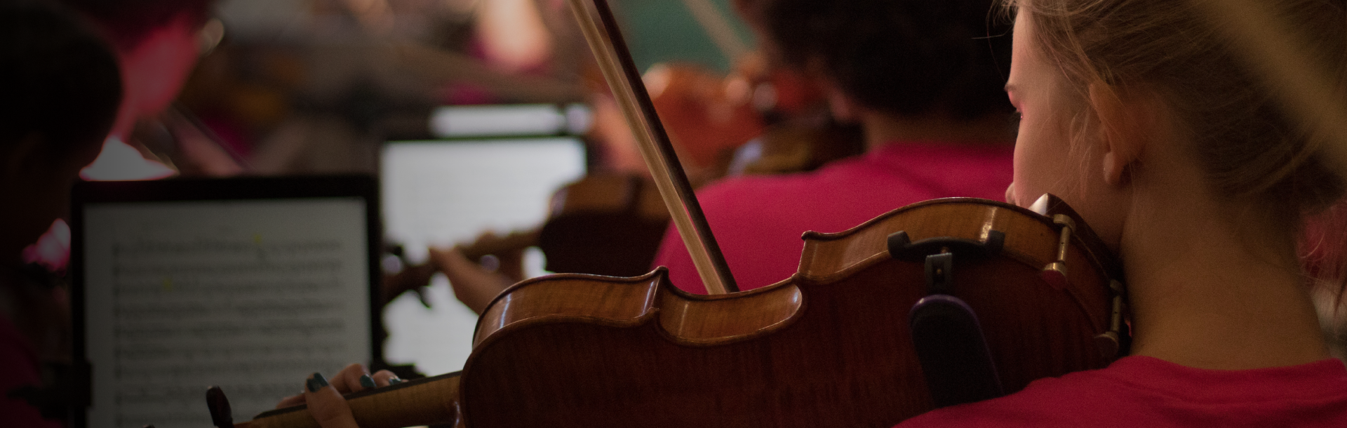 Over-the-shoulder image of students playing the violin and looking at music on iPads