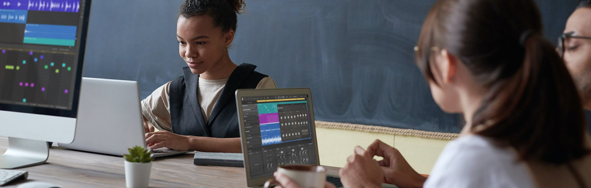 Three girls sitting around a table looking at laptops with Soundation Education on them. There is a chalkboard in the background.