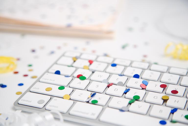 Computer keyboard on white desk covered in multi-colored confetti