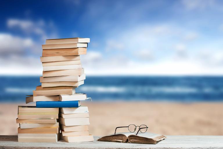 Stack of books with eyeglasses with beach in the background