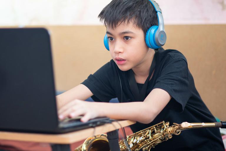 Boy with blue headphones on sitting in front of laptop with saxophone in his lap