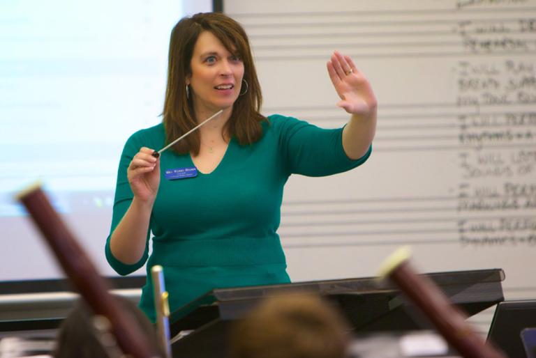 Wendy Higdon conducting her band ensemble in front of a smartboard and dry erase board.