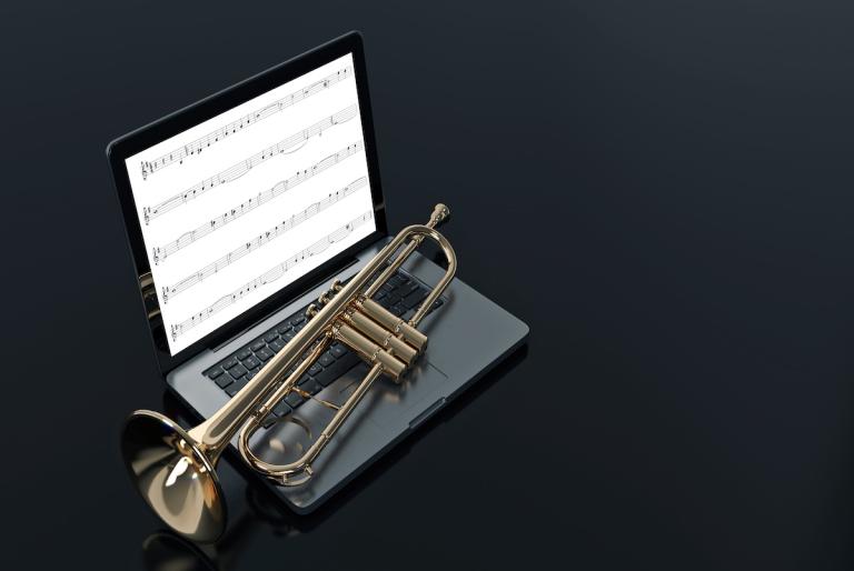 Trumpet on keyboard with sheet music displayed on laptop screen, solid dark grey background