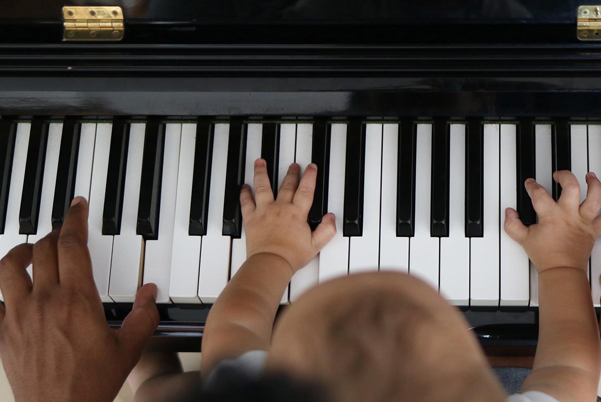 Toddler learning to play piano with father