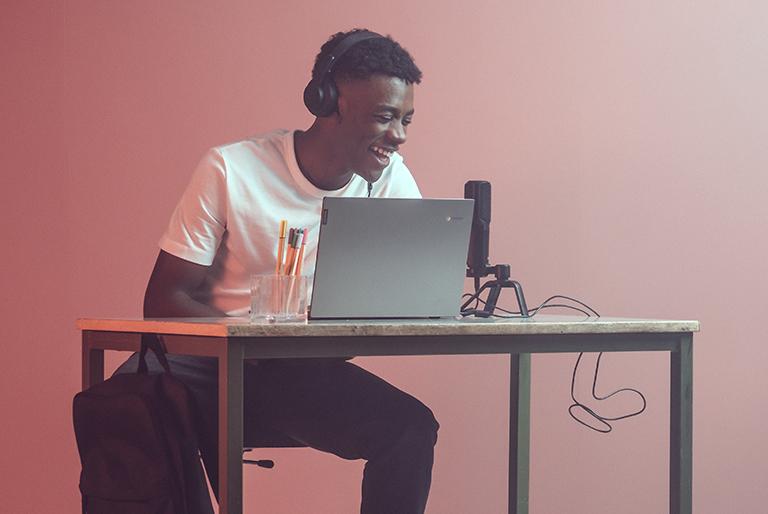 Student sitting at desk in front of a laptop recording audio into a microphone