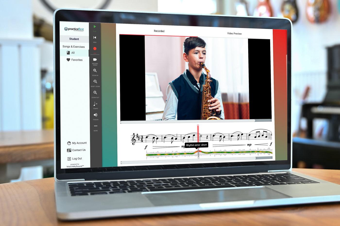 Laptop on desk with music classroom in the background. PracticeFirst software is shown on the laptop.