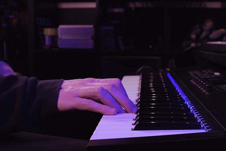 someone playing a digital keyboard, purple ambient light in a dark room