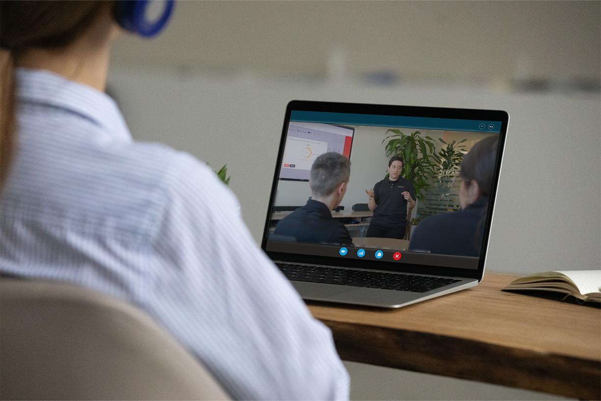 Over-the-shoulder view of woman sitting at laptop. Laptop is displaying MusicFirst support team giving a presentation.