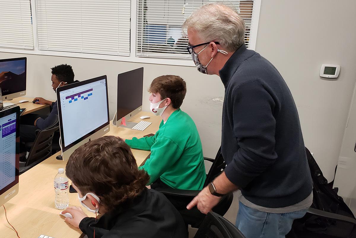 Teacher Brad Davis standing behind two students in front of computers. The computers are displaying the "Soundtrap for Education" software.