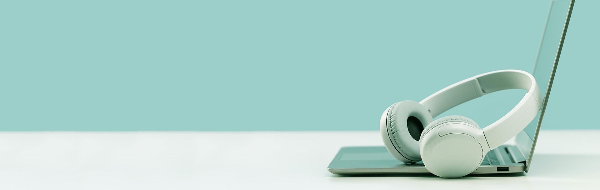 laptop with headphones sitting on white desk, aqua background